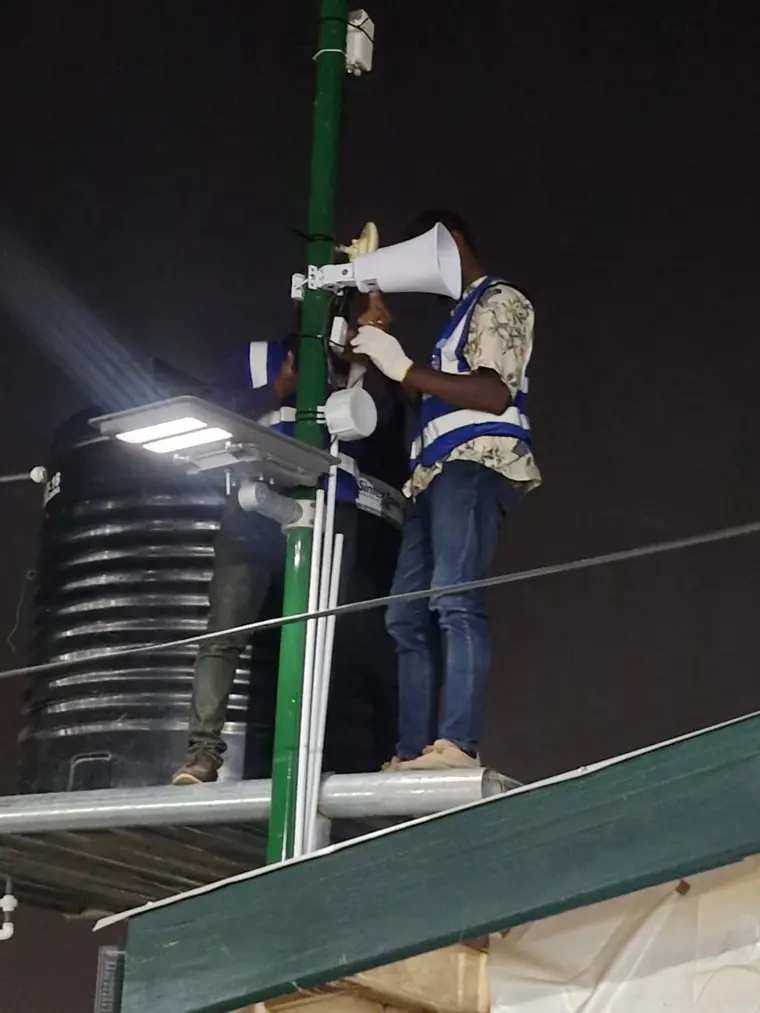 Two MulticomIoT technicians in hi-vis fitting a horn speaker to a mast after dark.