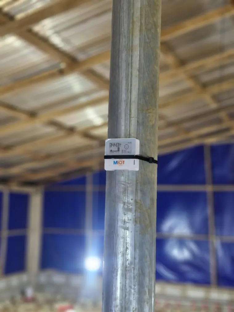 A MIOT temperature and humidity sensor with a small display, mounted on a pole in a poultry house.