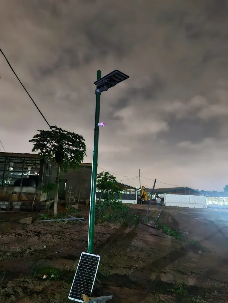 A solar-powered pole carrying a light and a camera at dusk on a farm site.